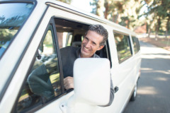 A smiling man leaning out the side of his car.