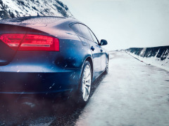 Image of a blue car driving down a snowy road, getting road salt on the cars undercarriage.