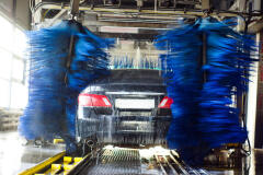 Black automobile going through automatic carwash with rotating blue neoprene washing cloths.