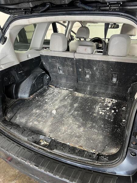 The back cargo area of an SUV before it had interior detailing from Andy's Autowash. It has chucks on debris & cake on dirt. 